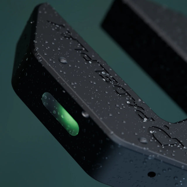 Close-up of a black padel electronic device with water droplets on a dark background
