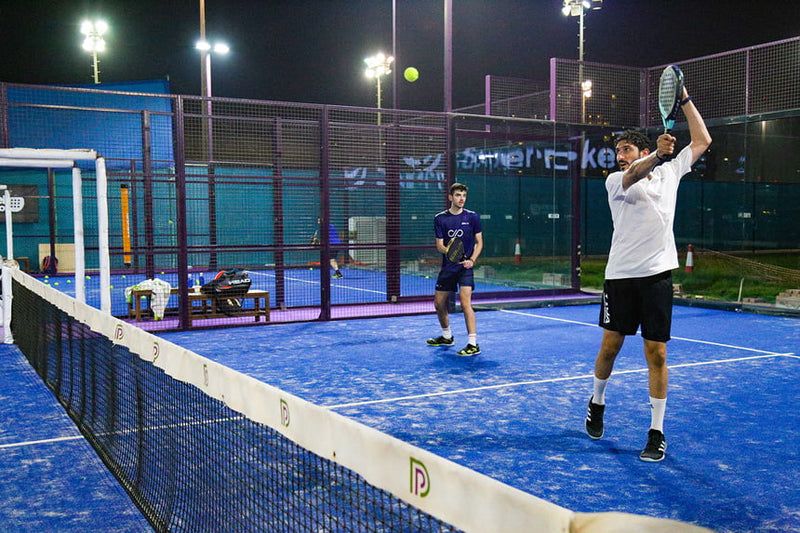 Two people playing padel on a blue court at night with lights illuminating the area.
